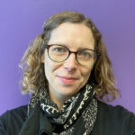 In this headshot, Gwen Hermanson is wearing a patterned neck scarf, a black top, and glasses against a purple background.